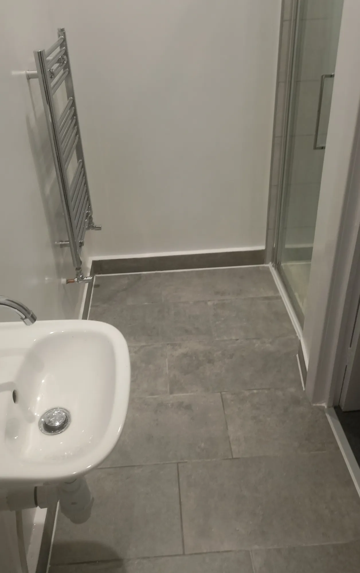 Compact shower room with basin, towel radiator and tiled floor.