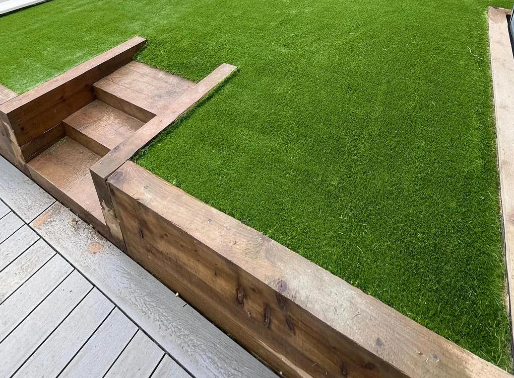 Timber-edged steps, lawn and decking within a landscaped garden.