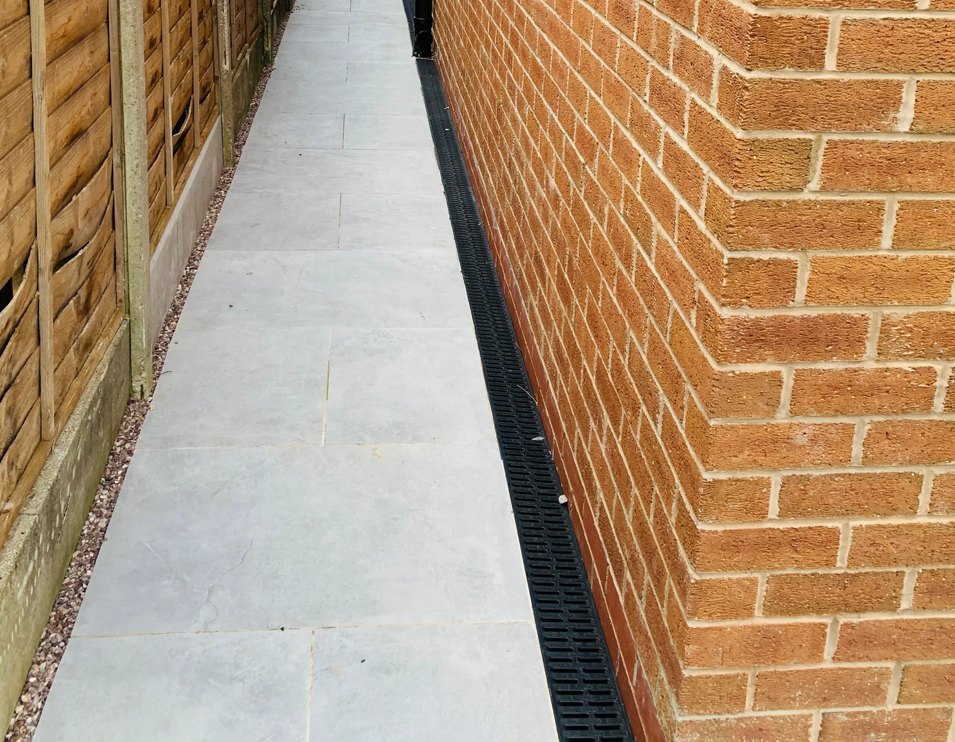 Narrow paved side access with brickwork, fencing and channel drainage.